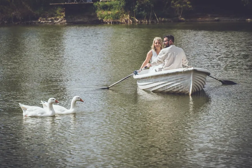 Cuplu într-o barcă albă, pe un lac cu lebede în apropiere