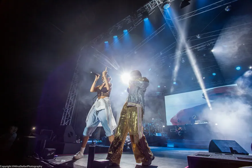 Două artiste pe scenă în costume strălucitoare, surprinse în timpul spectacolului