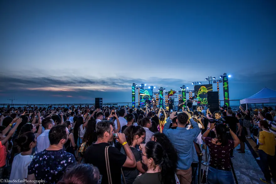 Mulțime adunată în fața unei scene de festival în lumina albastră a serii
