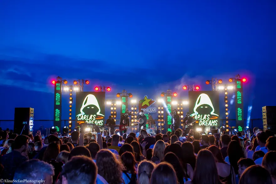 Imagine panoramică de festival cu lumini multicolore pe scenă și public pe întuneric