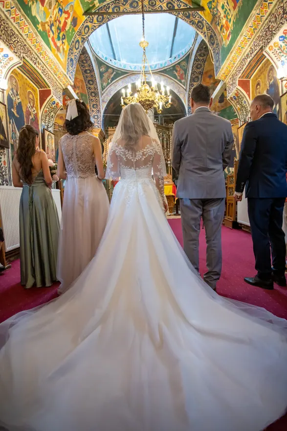 Mireasă cu rochie lungă fotografiată din spate într-un interior de ceremonie decorat