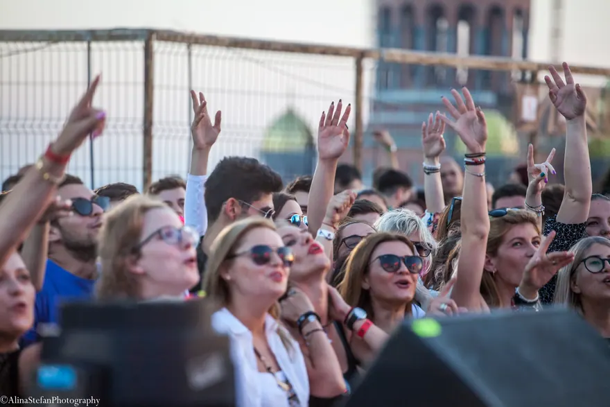 Spectatori apropiați de scenă cu mâinile ridicate, surprinși la un concert în aer liber