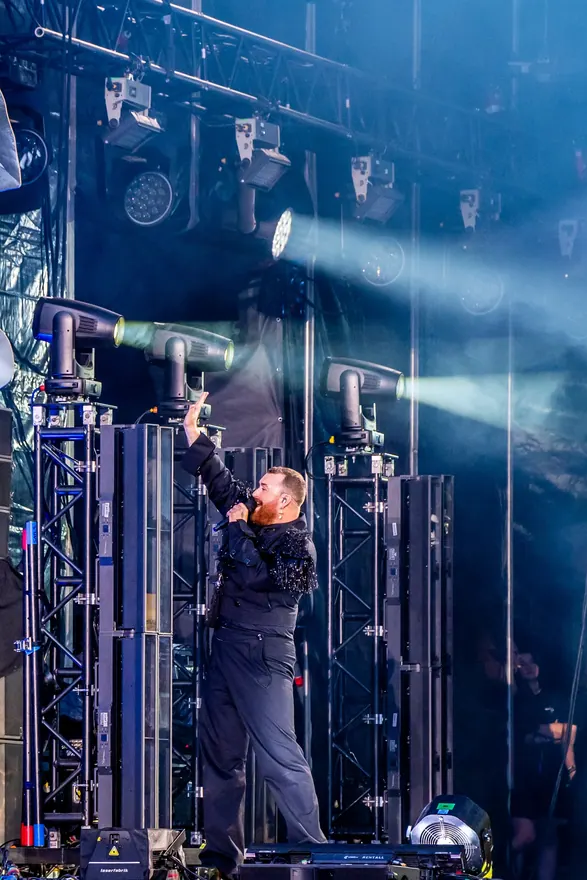Solist fotografiat vertical, înconjurat de structuri și reflectoare de concert