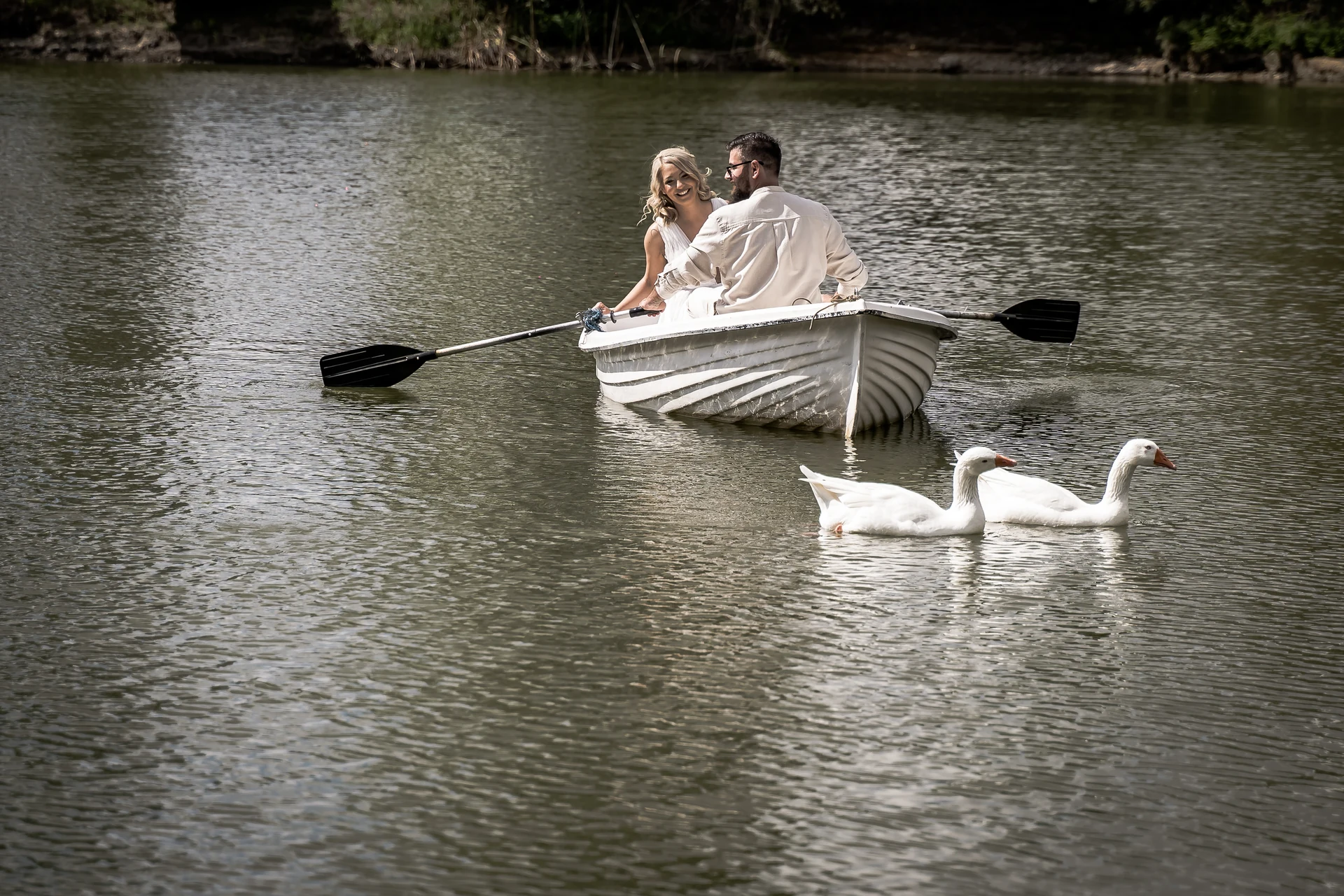 A wedding couple in a boat with two white geese on the lake, photograph by Alina Ștefan